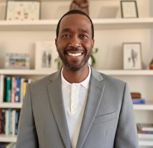 Image shows an attorney wearing a white shirt and a gray jacket with a blurred bookshelf in the background.